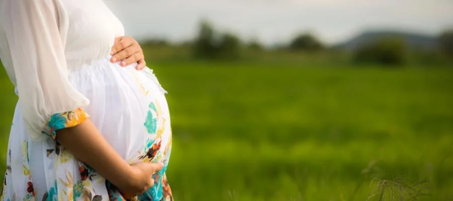 ‘Best of’ AHA's Advancing Health podcast highlights workforce wellness, rural obstetric services. A pregnant woman in a flowered dress stands in profile with a farm field behind her.