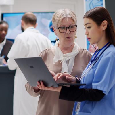 Senior nurse manager helping younger nurse analyze laptop